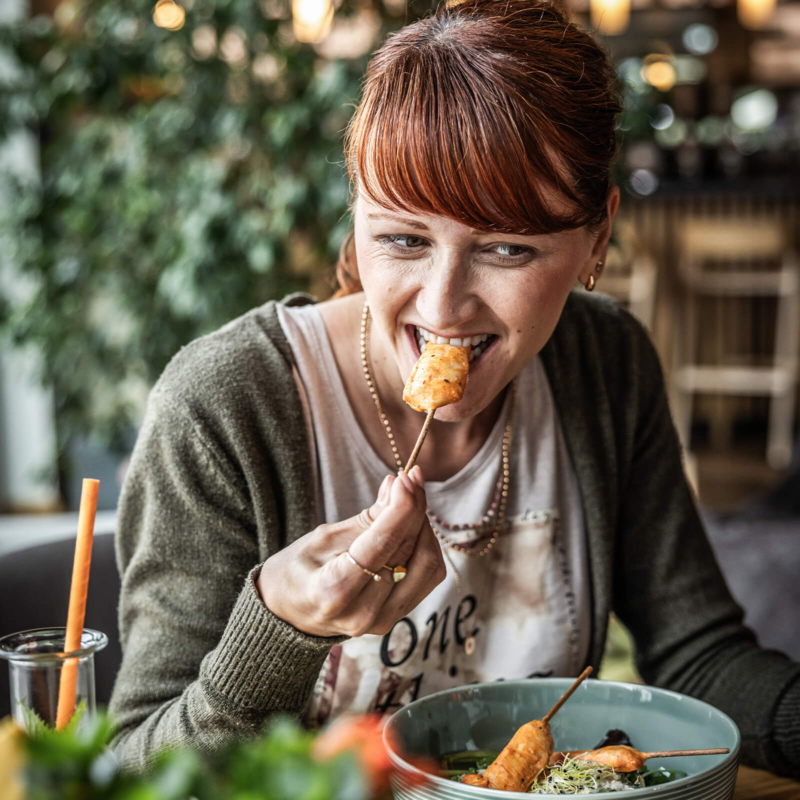 frau schmeckt haehnchenspies und geniest eine frisch zubereitete bowl im restaurant