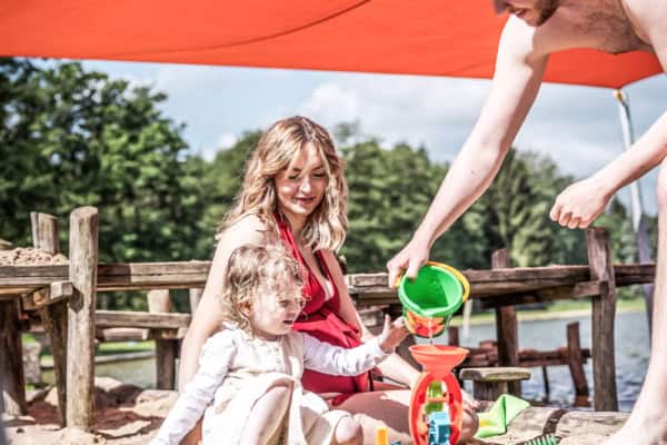 familie-auf-matschspielplatz-mit-sonnensegel-waldstrandbad-trixi-bad-grossschoenau Wassermatschspielplatz mit Überdachung im Waldstrandbad Grossschoenau