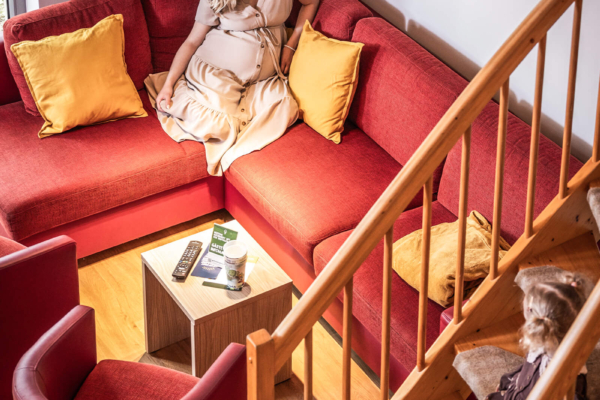 ferienhaus-mit-couch-zum-entspannen-trixi-park-zittauer-gebirge-typ-a Frau sitzt gemuetlich auf roter Couch im Ferienhaus
