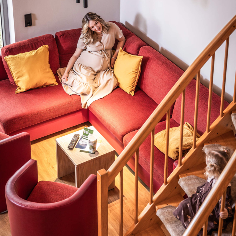 Frau sitzt gemuetlich auf roter Couch im Ferienhaus