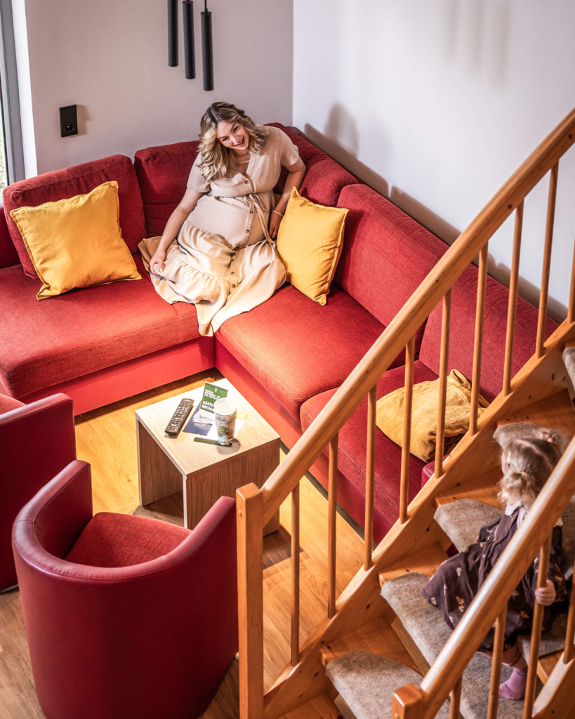 ferienhaus-mit-couch-zum-entspannen-trixi-park-zittauer-gebirge-typ-a Frau sitzt gemuetlich auf roter Couch im Ferienhaus
