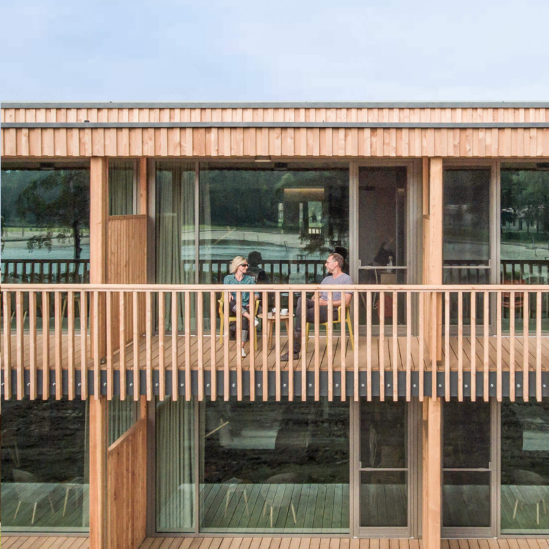 hotel-ansicht-balkone-mit-bestuhlung-trixi-park-zittauer-gebirge Aussenansicht mit 2 Personen auf Balkon im Waldstrand-Hotel